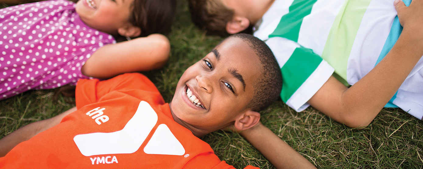 kids lying on the grass smiling and wearing YMCA shirts