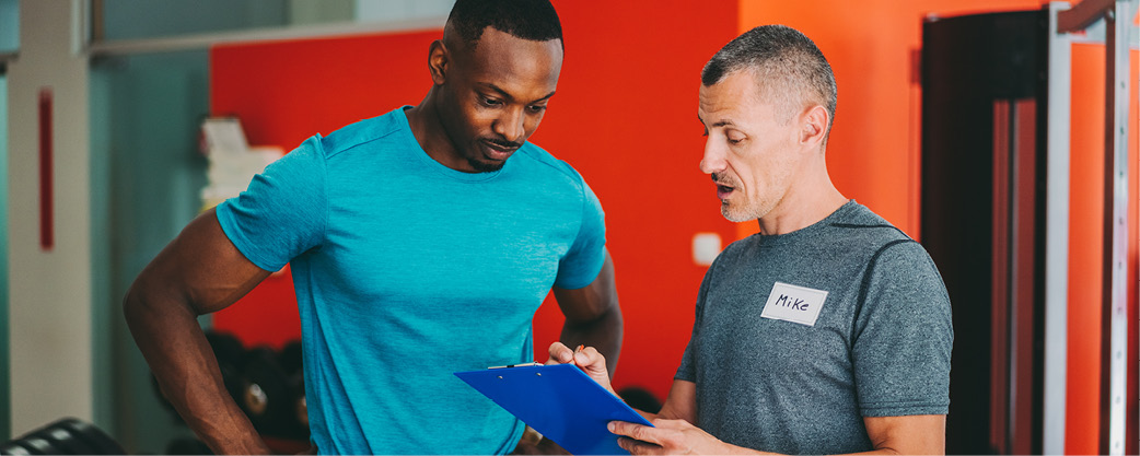 Man with clipboard offering coaching to a man working out