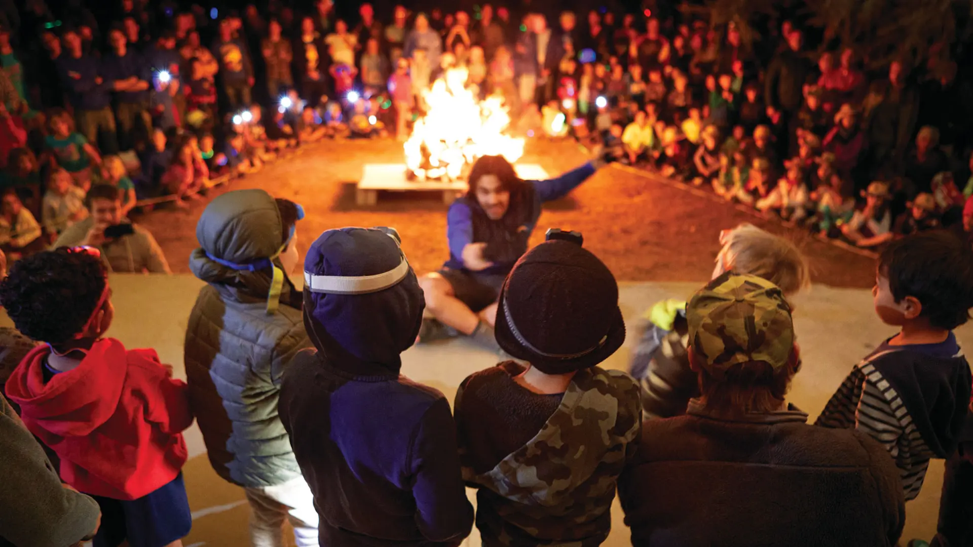 Camp Loma Mar counselor telling a story at night to a group of campers around the fire pit