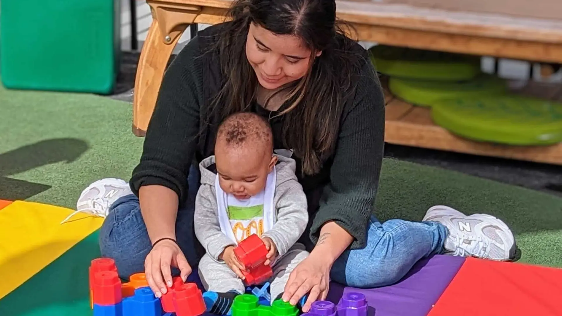YMCA Cherryland Early Learning Center teacher with a small infant playing with blocks on the outdoor playground