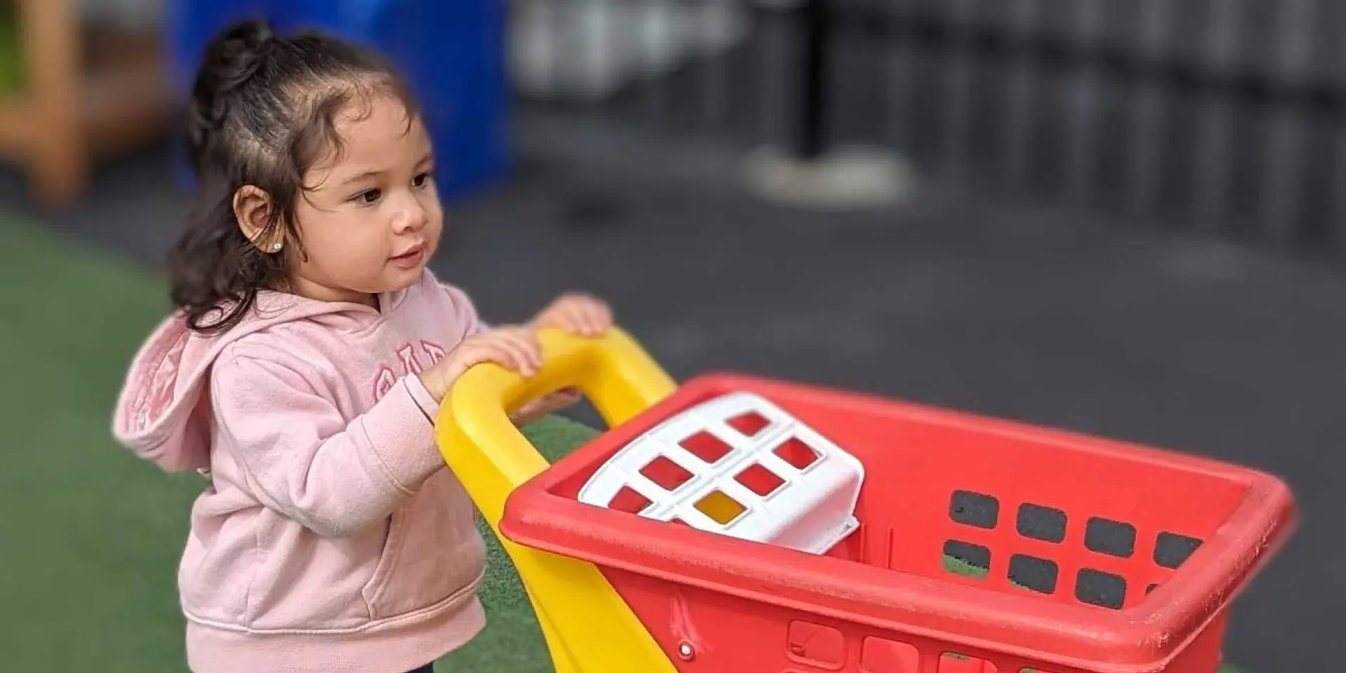 Early Learning Center female toddler playing with a toy shopping cart on outdoor playground