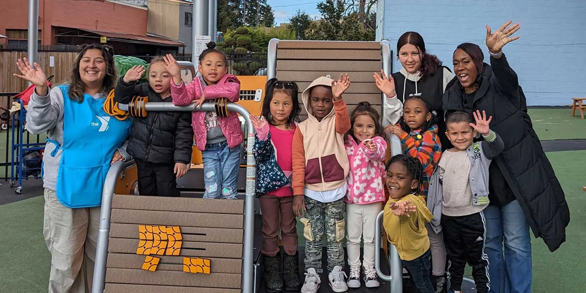 group of preschoolers at the Cherryland Early Learning Center smiling and waving with their teachers on the outdoor playground