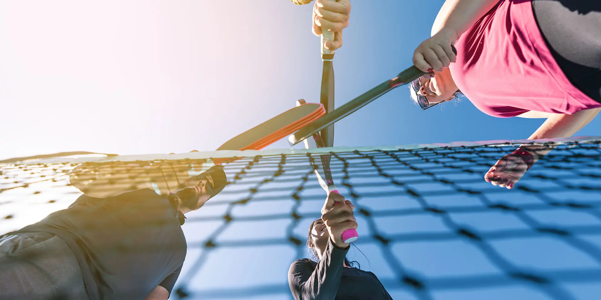 Pickleball players with paddles over net on an outdoor pickleball court