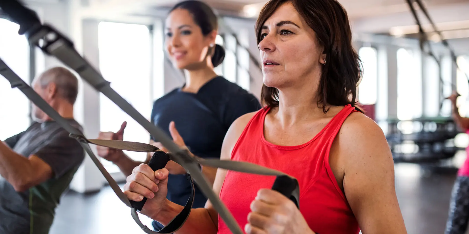 mid age woman in group exercise TRX class with trainer