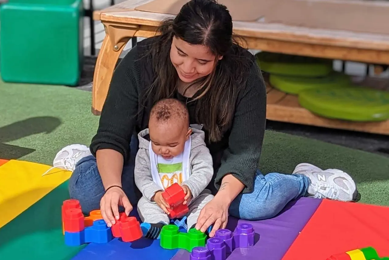 YMCA Cherryland Early Learning Center teacher with a small infant playing with blocks on the outdoor playground