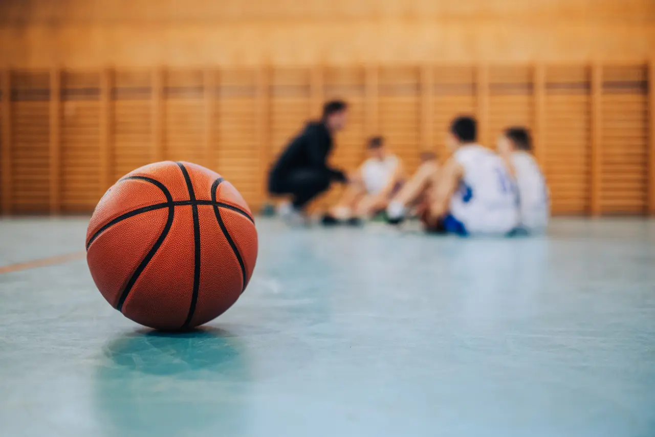 Basketball on court in foreground with teammates circled up in the background
