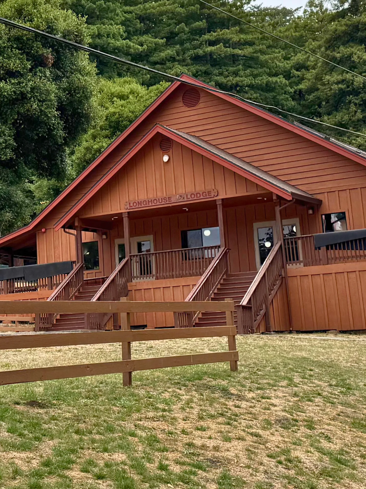The Camp Loma Mar lodge sits in front of large evergreen trees, a red fence sits in front of the lodge.