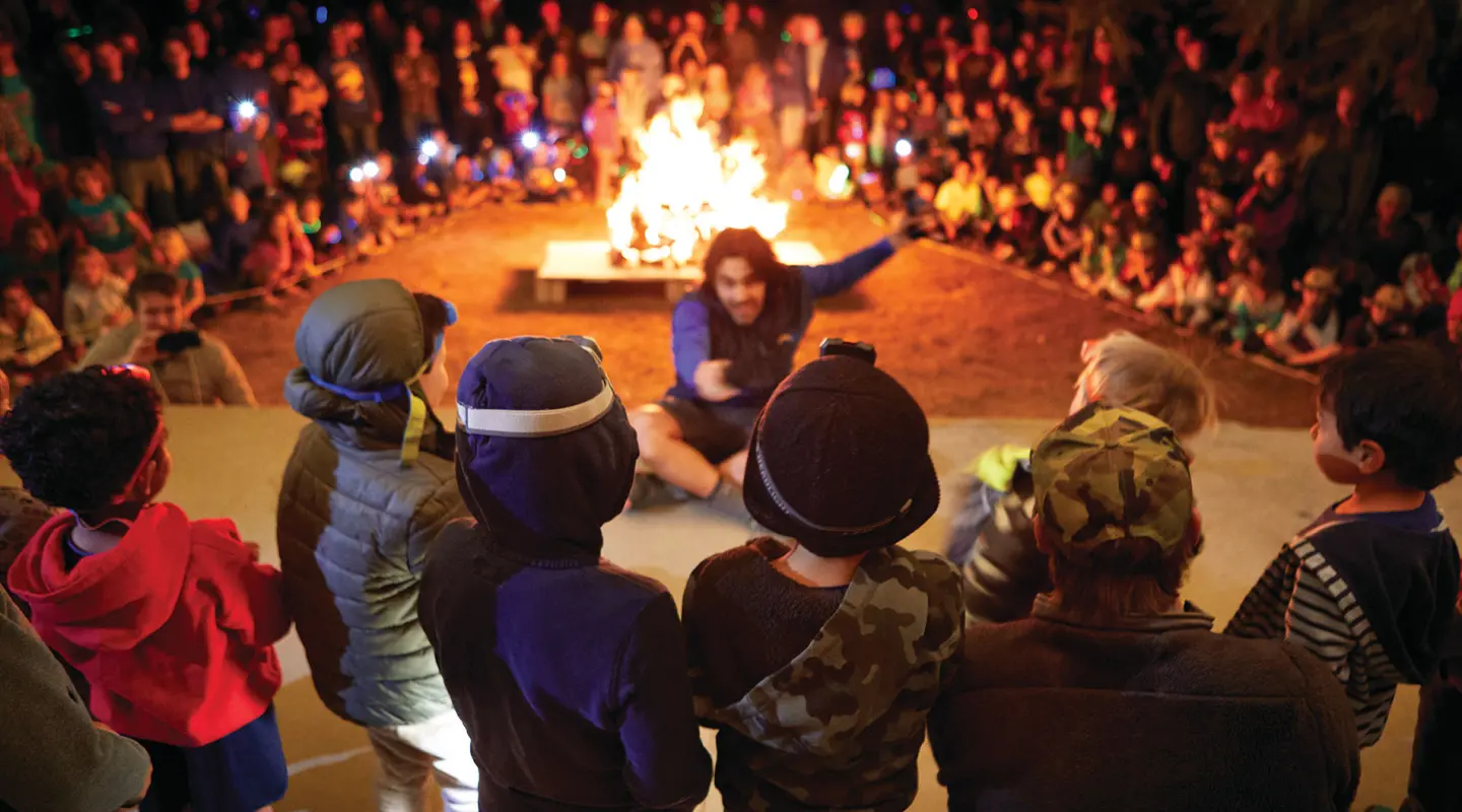 Camp Loma Mar counselor telling a story at night to a group of campers around the fire pit