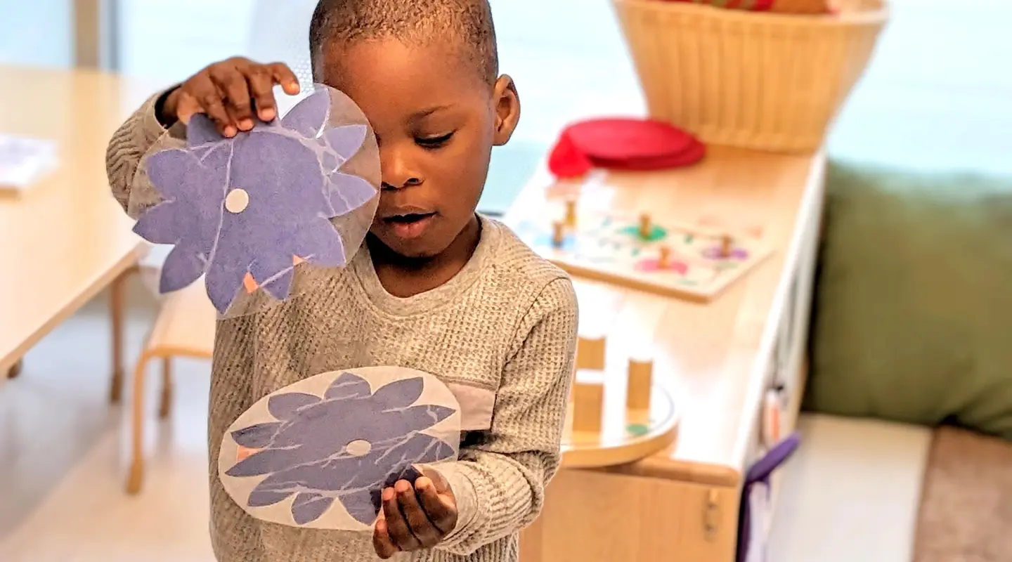 Preschool male student showing and playing with paper artwork 