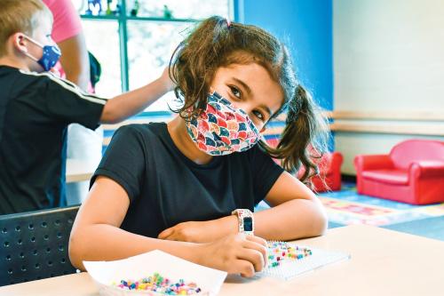 little girl with cute pigtails wearing a mask and doing bead work