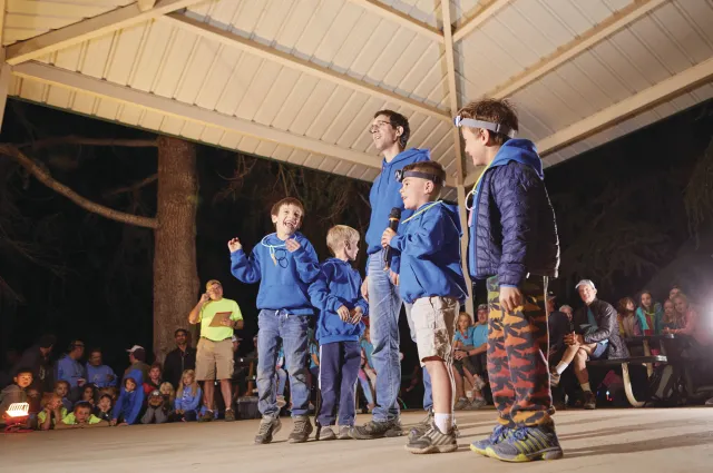 A family stands inside of the a gazebo at night while participating in family camp activities