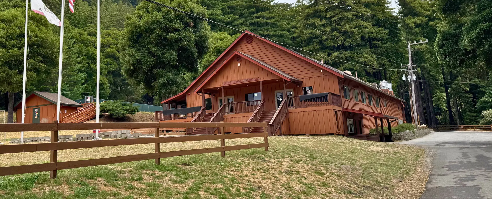 The Camp Loma Mar lodge sits in front of large evergreen trees, a red fence sits in front of the lodge.