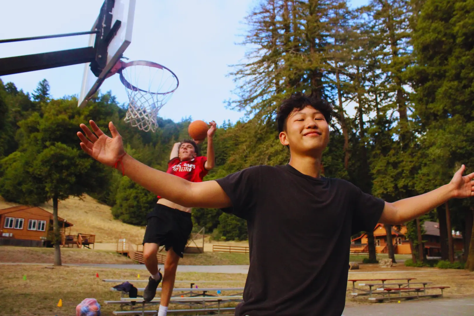 Two boys play basketball, one of them runs away from the basket with his arms outstretched while his friend flies through the air to dunk the ball behind him, recreating an iconic picture of Lebron James and Dwyane Wade on the Miami Heat.