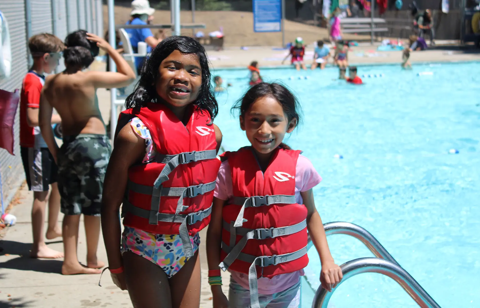 smiling young female campers in front of pool with life vests on