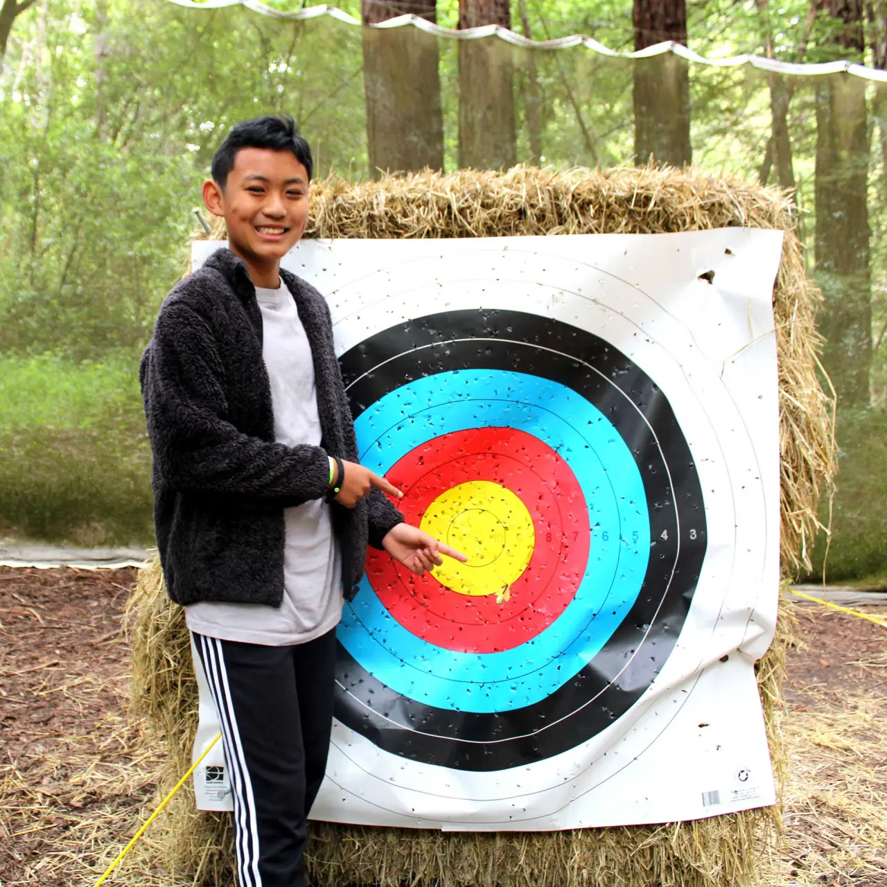 Camp Loma Mar male camper smiling and pointing at the archery target with bullseye