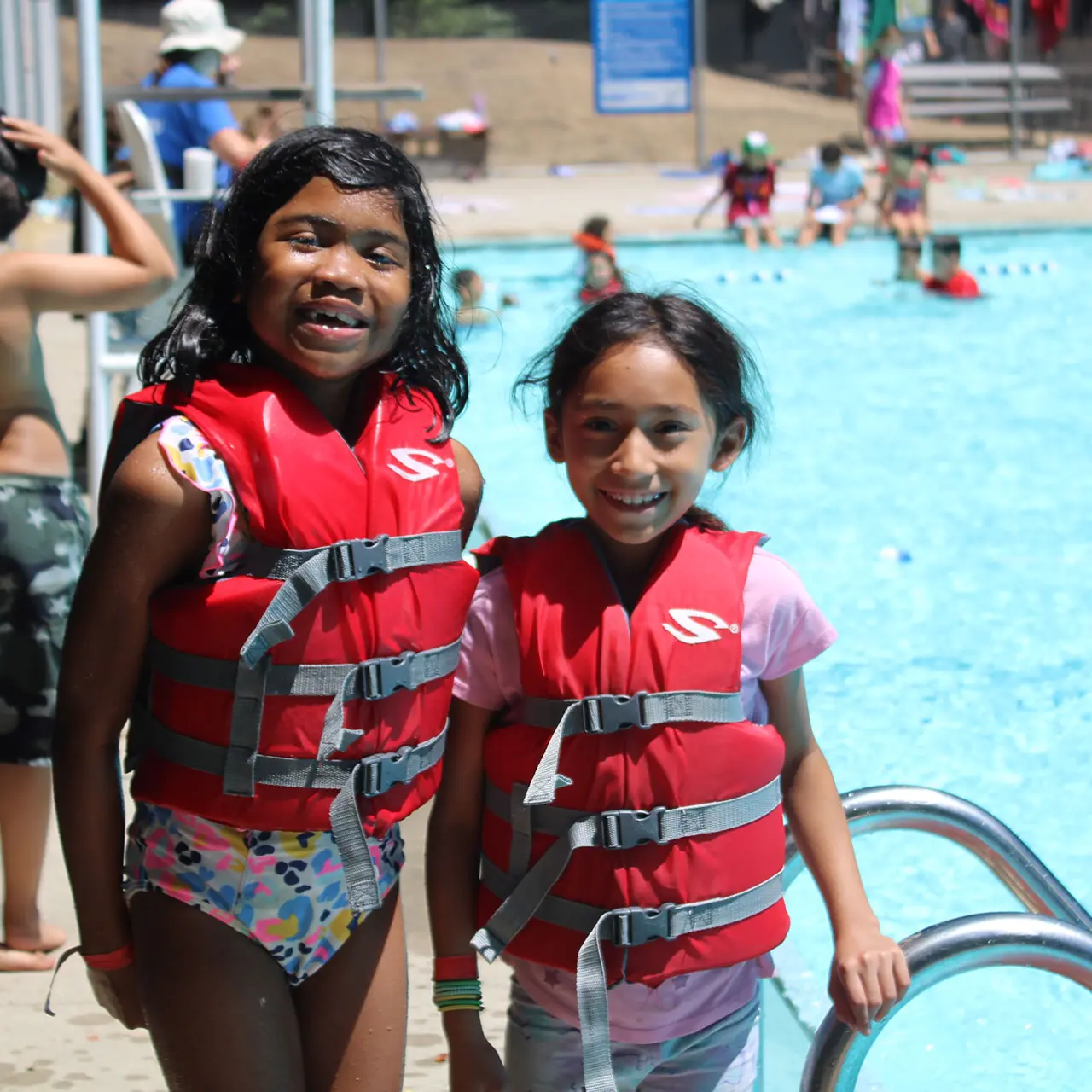 smiling young female campers in front of pool with life vests on