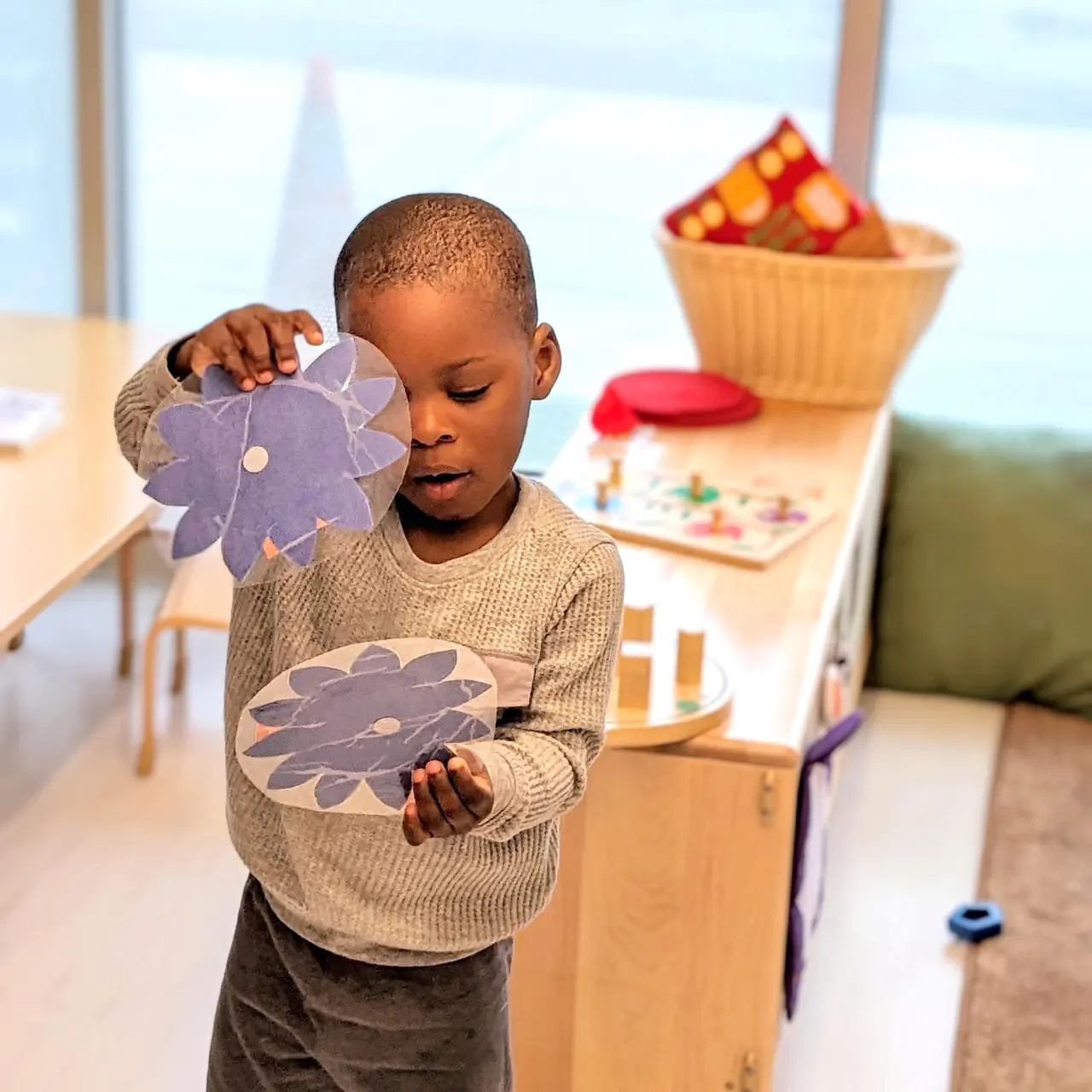 Preschool male student showing and playing with paper artwork 