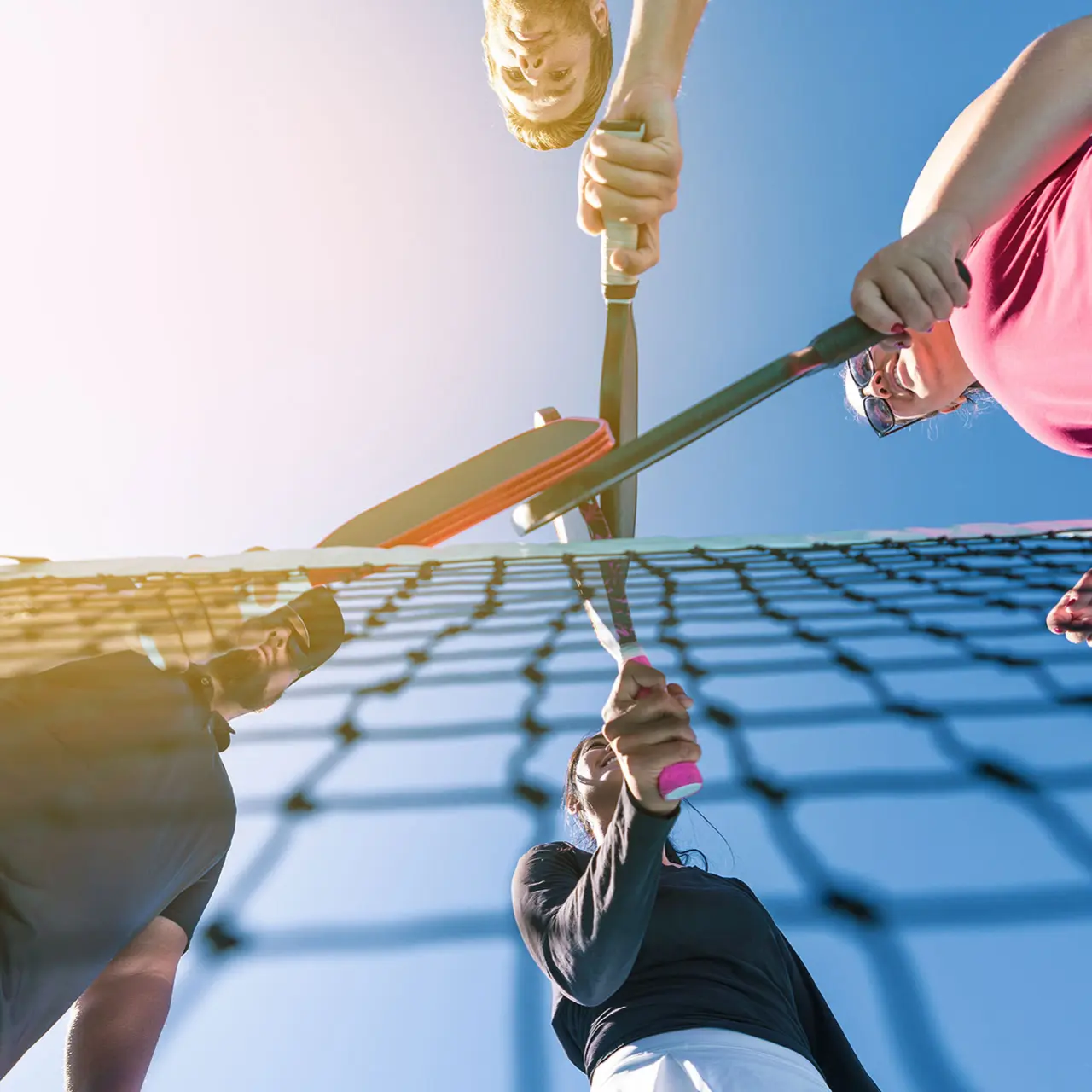 Pickleball players with paddles over net on an outdoor pickleball court