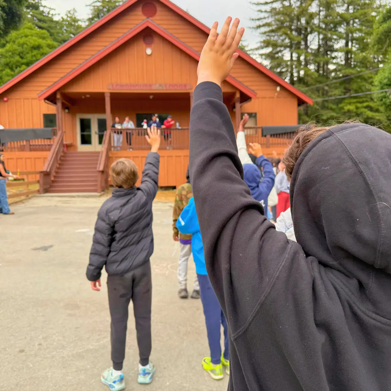 Two boys in black jackets raise their hands in the lunch line in front of the Camp Loma Mar lodge.