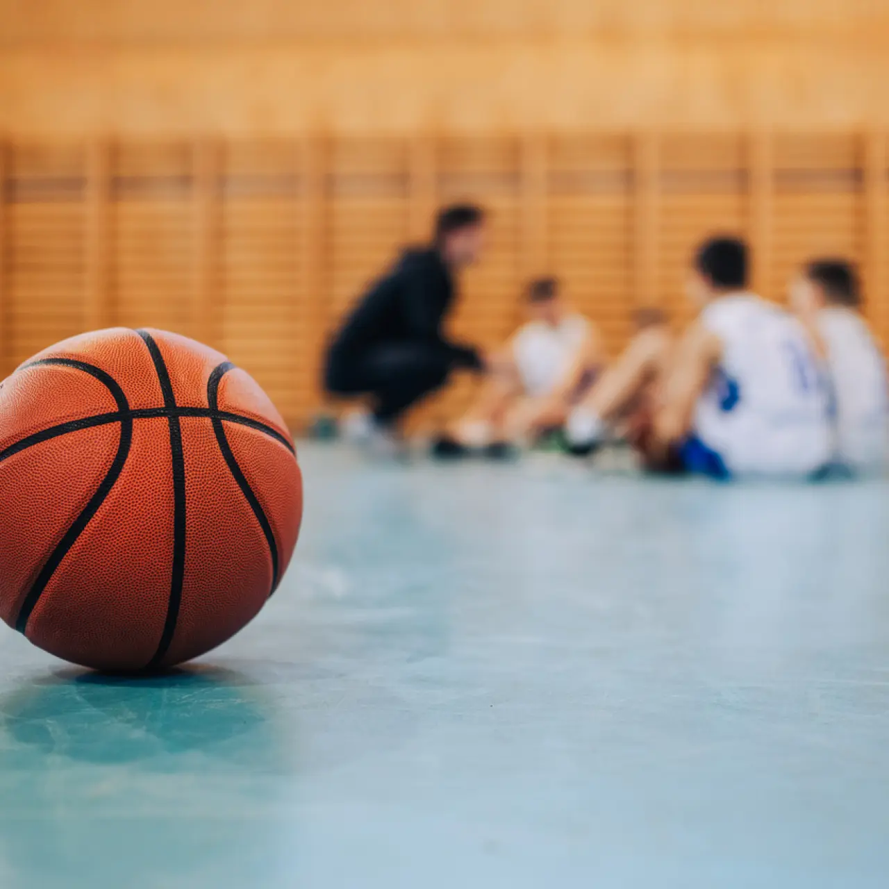 Basketball on court in foreground with teammates circled up in the background
