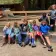 8 campers smile and wave at the camera while sitting on stepped benches in a recreation area in the woods at Camp Loma Mar.