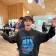 A boy in a black hoodie stretches his arms out in excitement for lunch in a cafeteria.