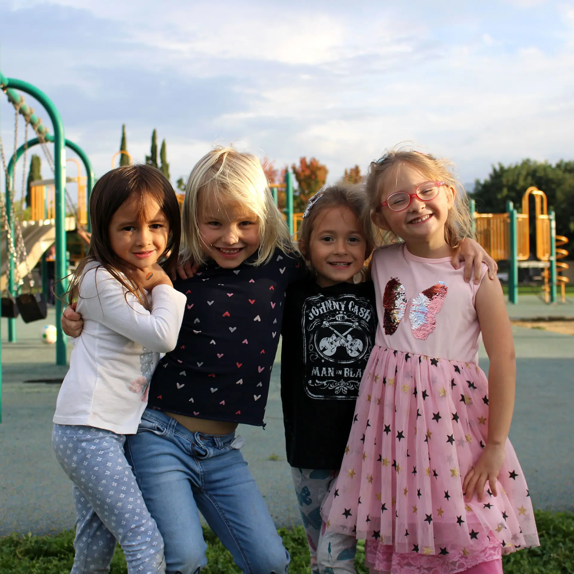 Group of young students smiling with arms around each other in front of outdoor playground structure 