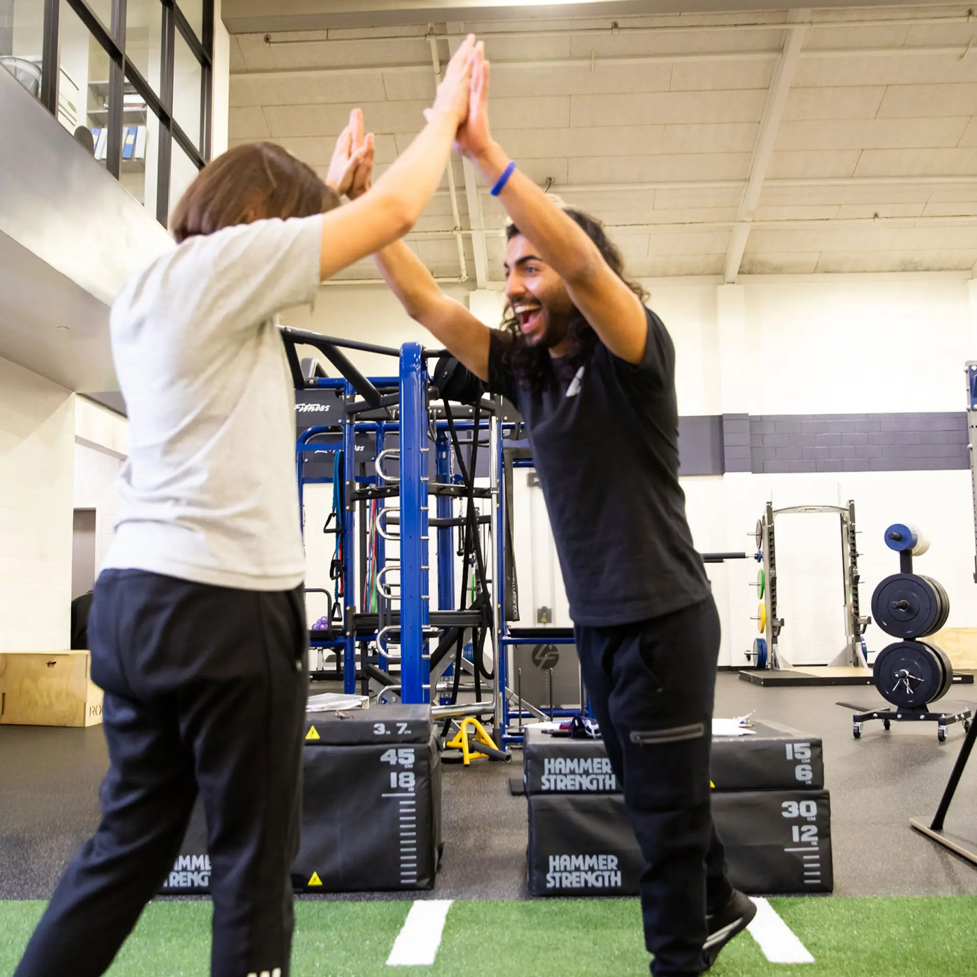 A personal trainer high fives client on turf area