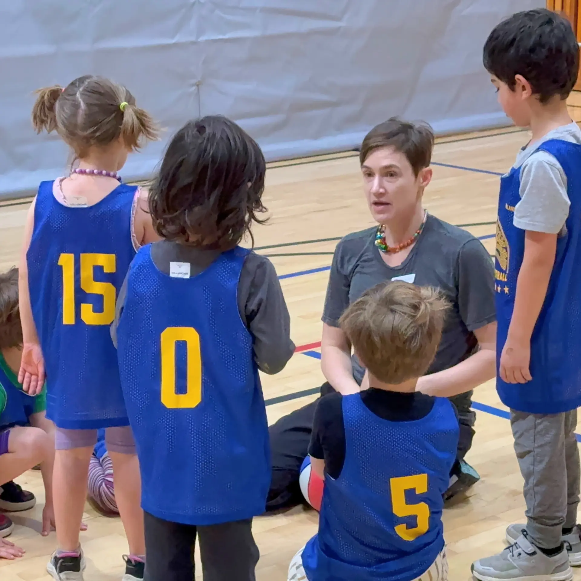 Kids gather around their basketball coach for a huddle to strategize during a basketball game.